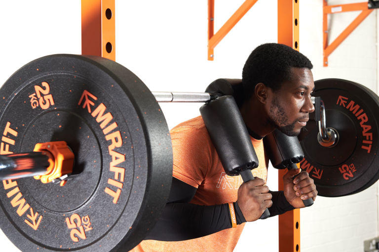Man doing squats with a Mirafit 7ft Olympic Safety Squat Bar