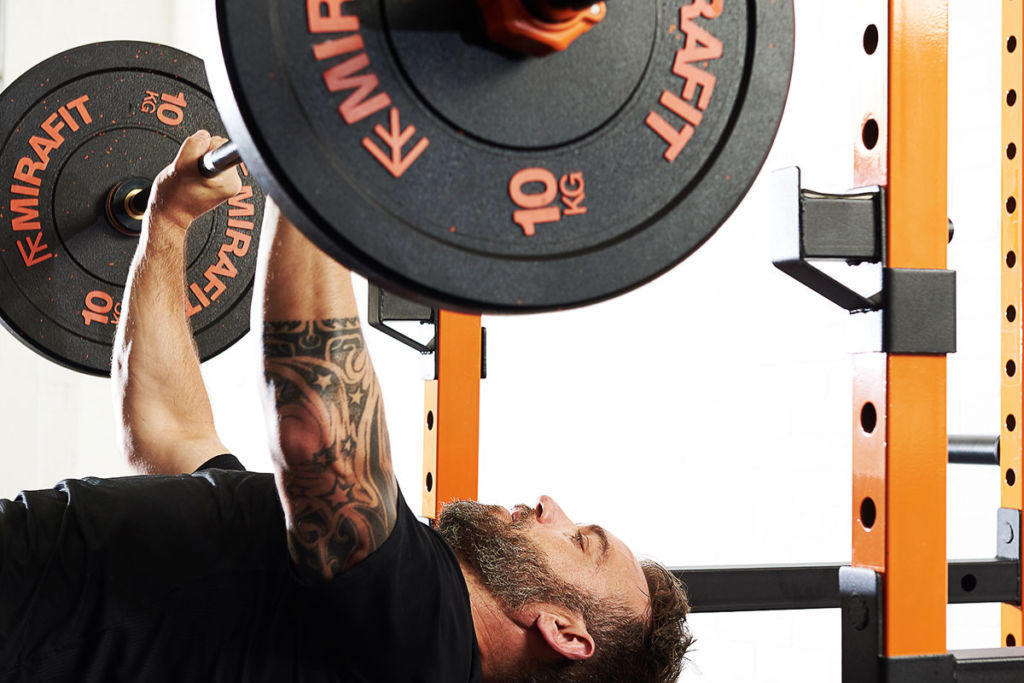 Mirafit Crumb Rubber Olympic Bumper Plates Man performing a bench press with Mirafit 10kg weight plates