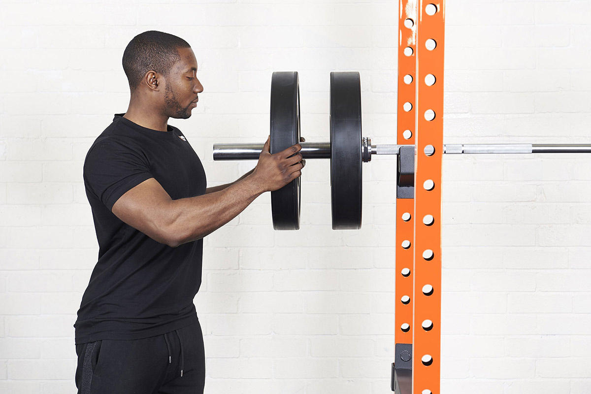 Man loading Mirafit Black Olympic Rubber Bumper Plates onto an Olympic barbell