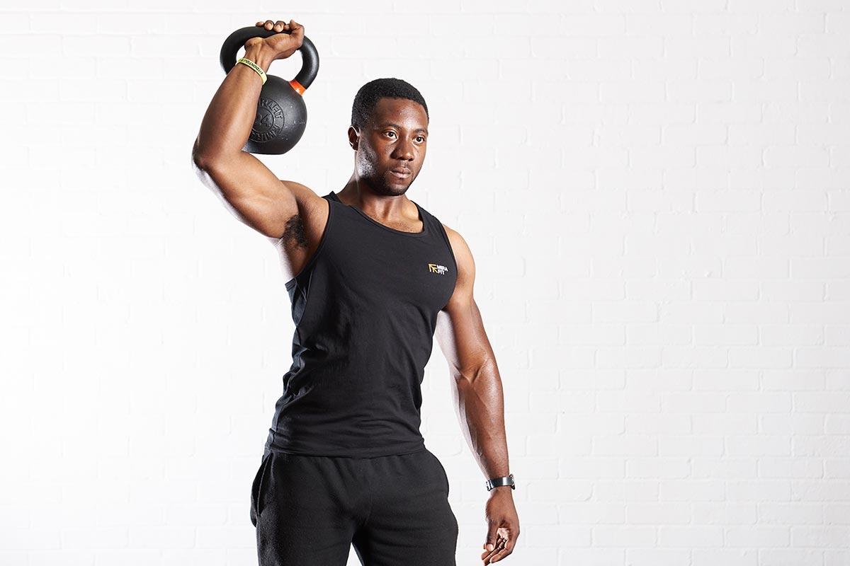 Fitness expert lifts a Mirafit kettlebell above his head while in the gym