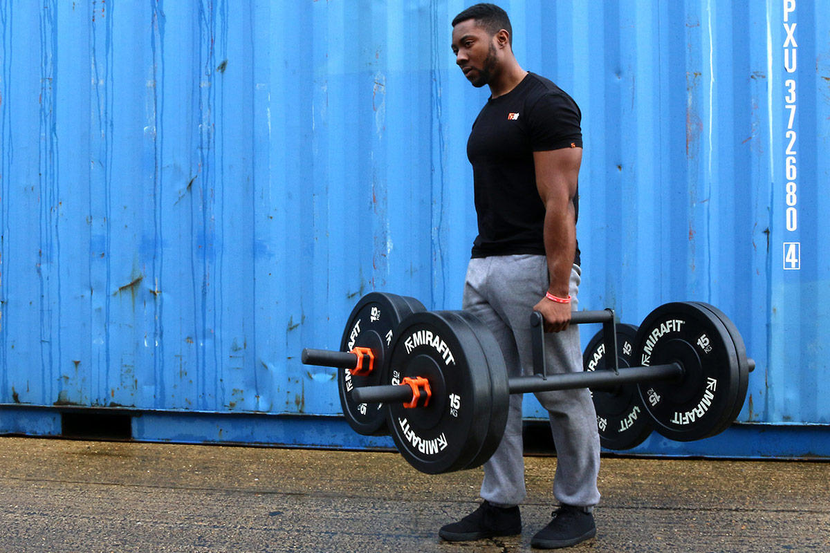 Mirafit Farmers Walk Handles Man performing a Farmers Walk with Mirafit Farmers Walk Handles. 15kg weight plates are visible.