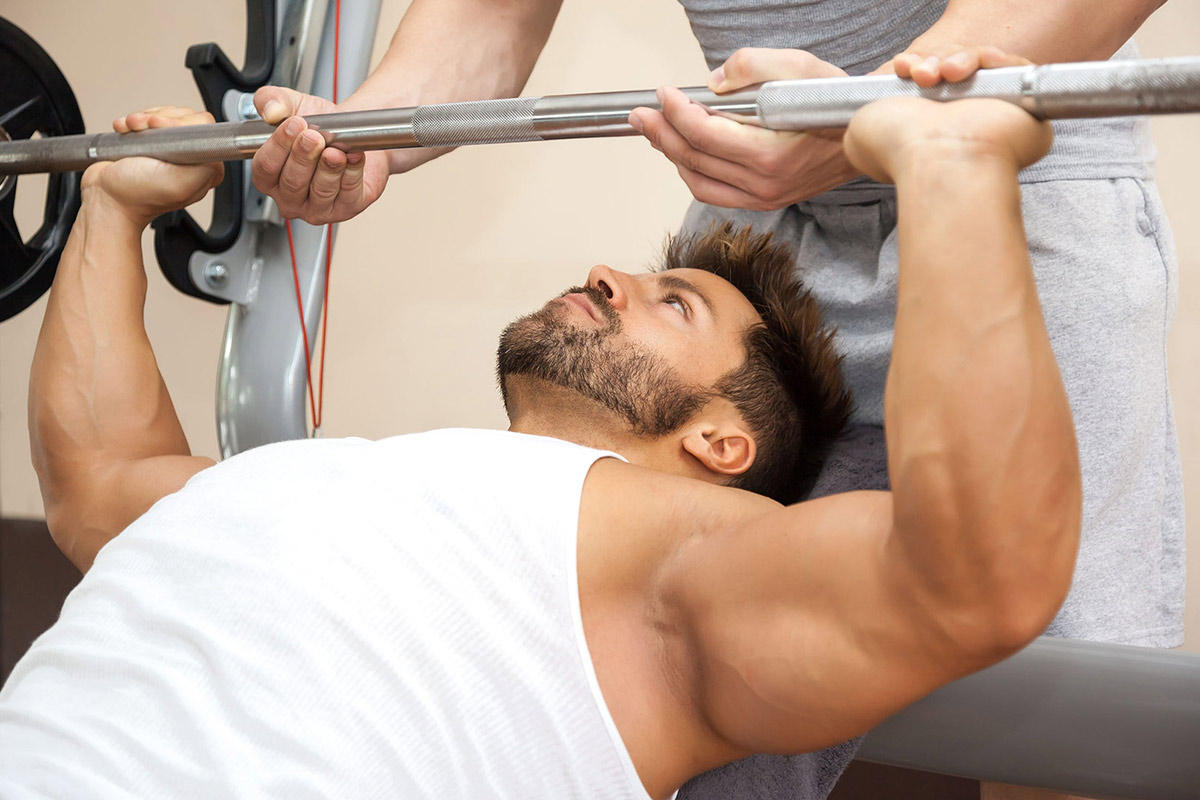 young man doing a chest press in the gym with a friend spotting him