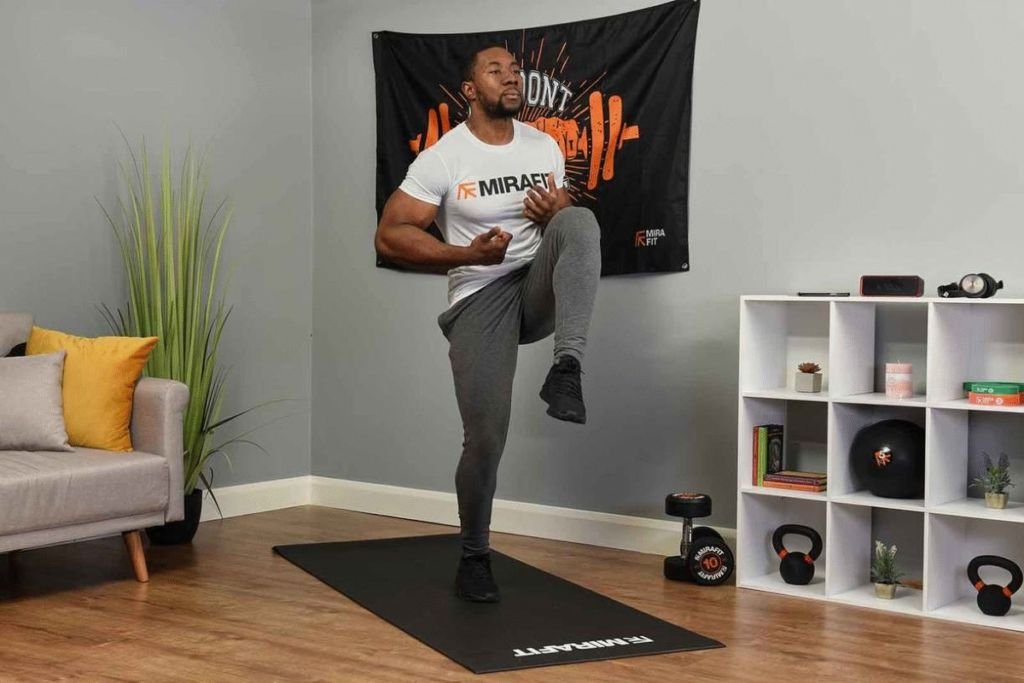 Man doing high knees in his home gym. A pair of 10kg dumbbells are behind him.