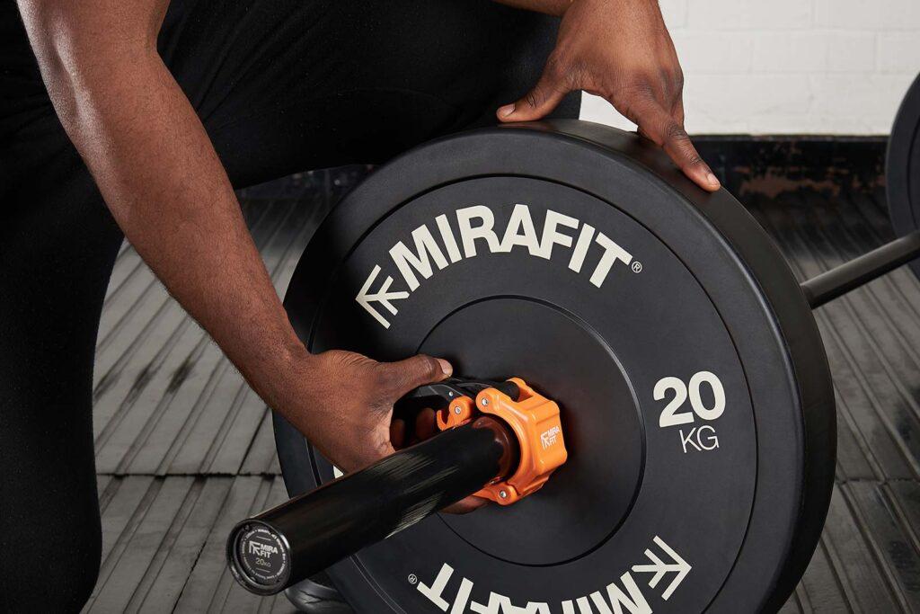 Mirafit Black Olympic Rubber Bumper Plates Man adding weight collars to Mirafit 20kg weight plates