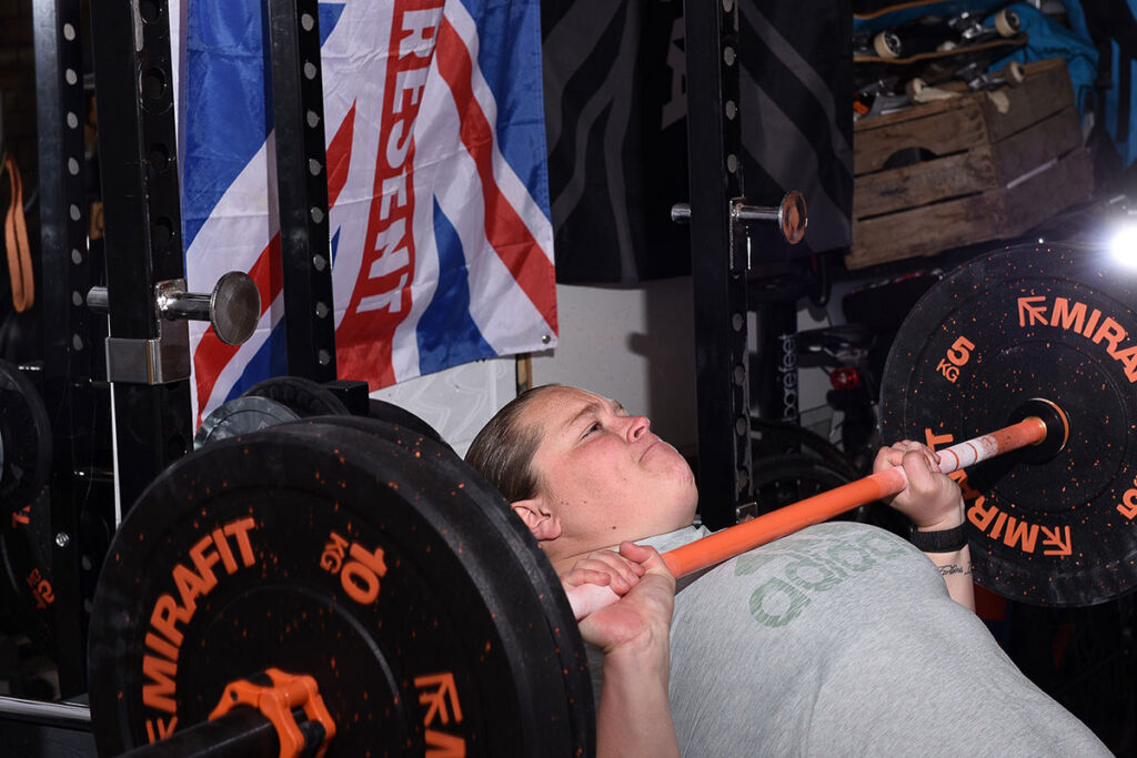 Sophie McKinna bench pressing a Mirafit women's barbell, 10kg weight plates and 5kg weight plates