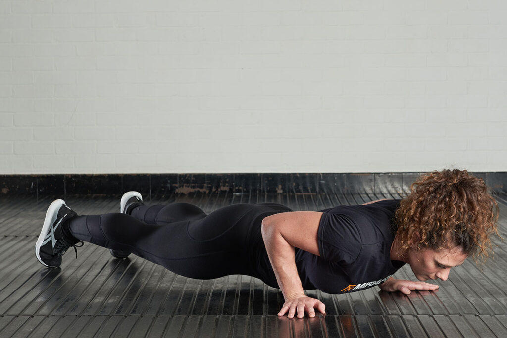 Mirafit Women's Black Gym T-Shirt A woman wearing a Mirafit shirt performs a push up on gym flooring