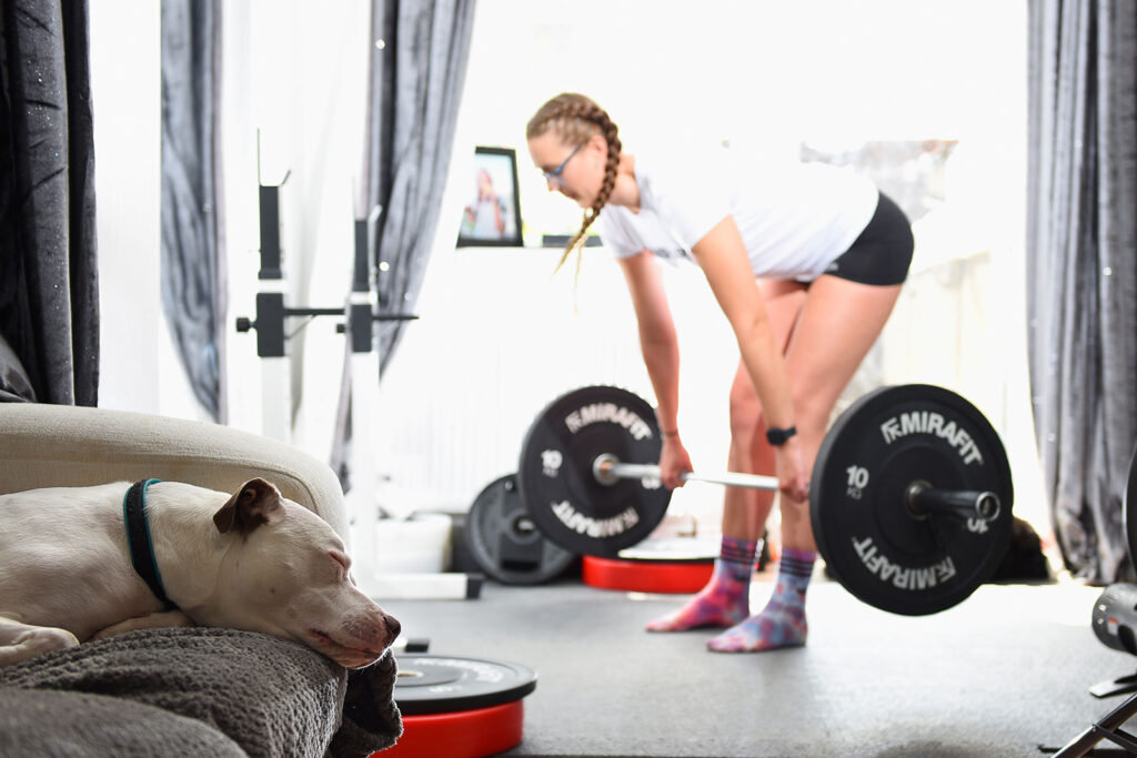 Paralympic Swimmer Jessica Jane Applegate deadlifting in her living room gym during lockdown with her dog in the picture