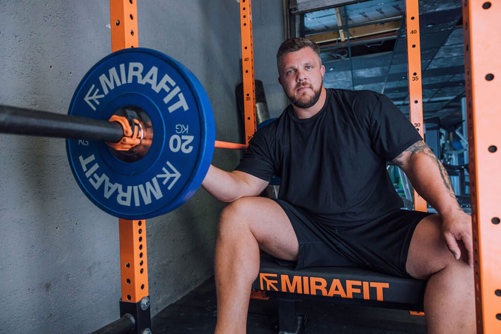 Mirafit M3 7ft 20kg Olympic Barbell Strongman Luke Stoltman sitting near a Mirafit M3 7ft 20kg Olympic Barbell
