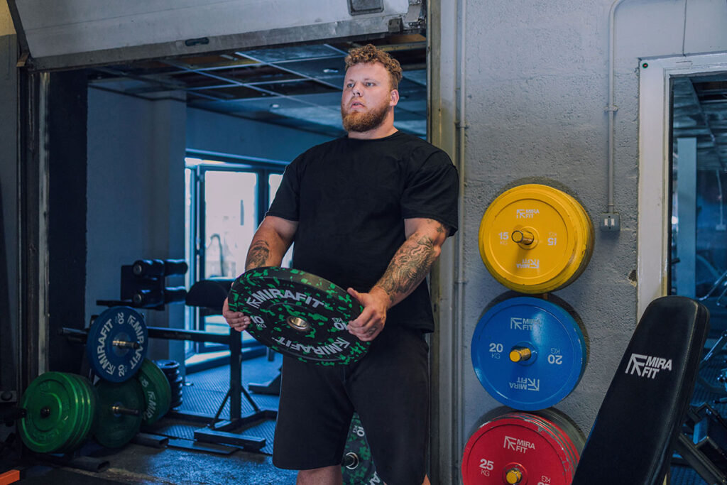 Mirafit Extra Thin Steel Coloured Olympic Plates WSM 2021 Winner Tom Stoltman performing a delt raise with a Mirafit colour splash bumper plate