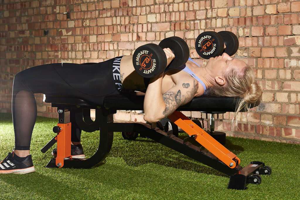 Mirafit M150 Adjustable Weight Bench Woman performing a dumbbell bench press with Mirafit 12.5kg dumbbells