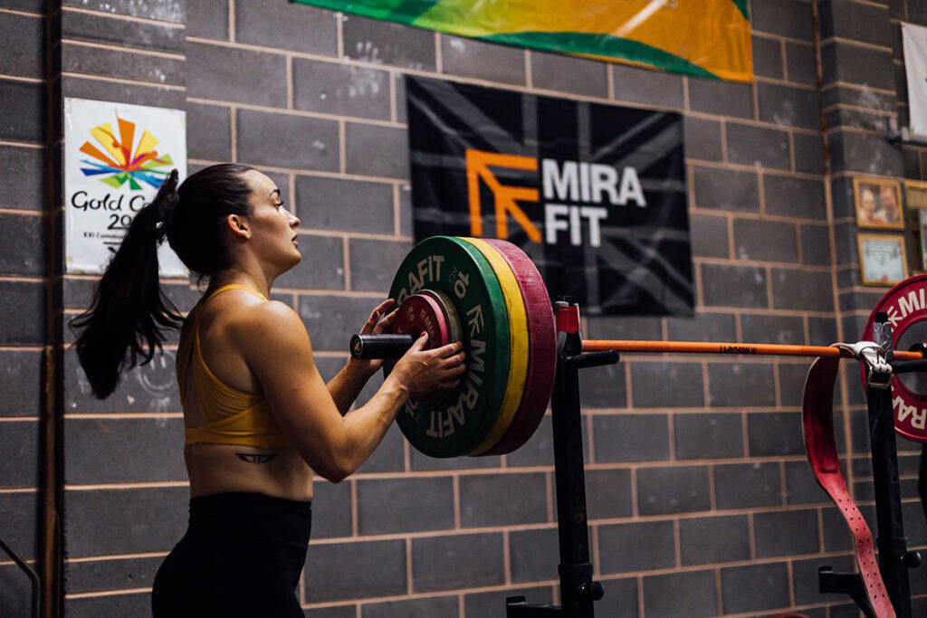 Mirafit M120 Adjustable Squat Rack Team GB Olympic Weightlifter Sarah Davies loading Mirafit weight plates onto a Mirafit women's Olympic barbell