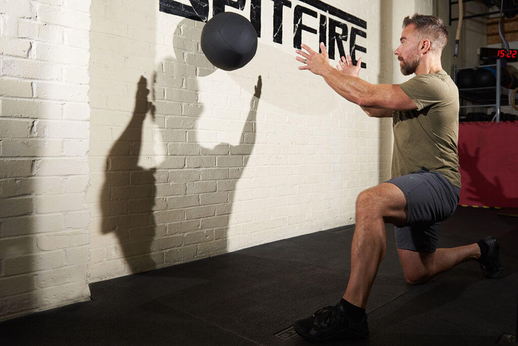 Man performing a half kneeling medicine ball throw with a Mirafit medicine ball. He is keeping his muscles tight, one of many medicine ball benefits.