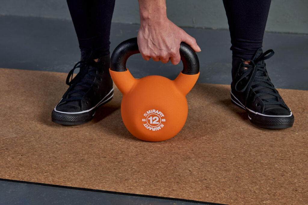Mirafit Soft Touch Cast Iron Kettlebell - 12kg Kettlebell Woman gripping a Mirafit 12kg kettlebell