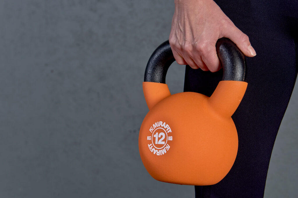 Mirafit Soft Touch Cast Iron Kettlebell - 12kg Kettlebell Woman grasping a Mirafit 12kg kettlebell in one hand