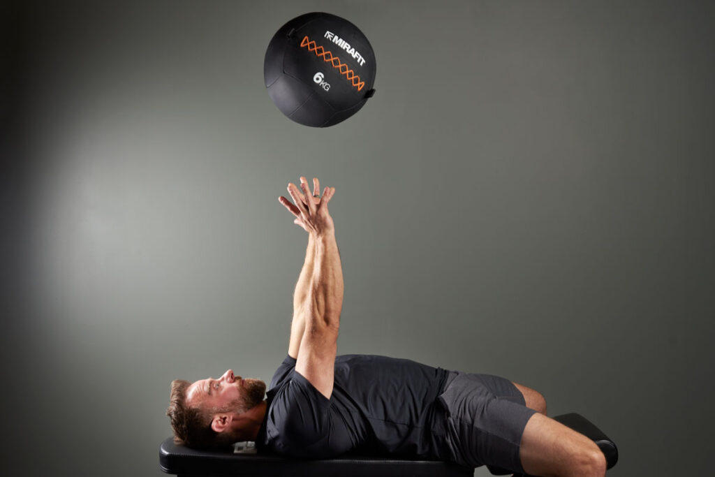 Mirafit Gen III Stitched Medicine Wall Ball - 6kg Wall Ball Man Performing a Medicine Ball Bench Throw With a Mirafit Gen III Stitched Medicine Wall Ball