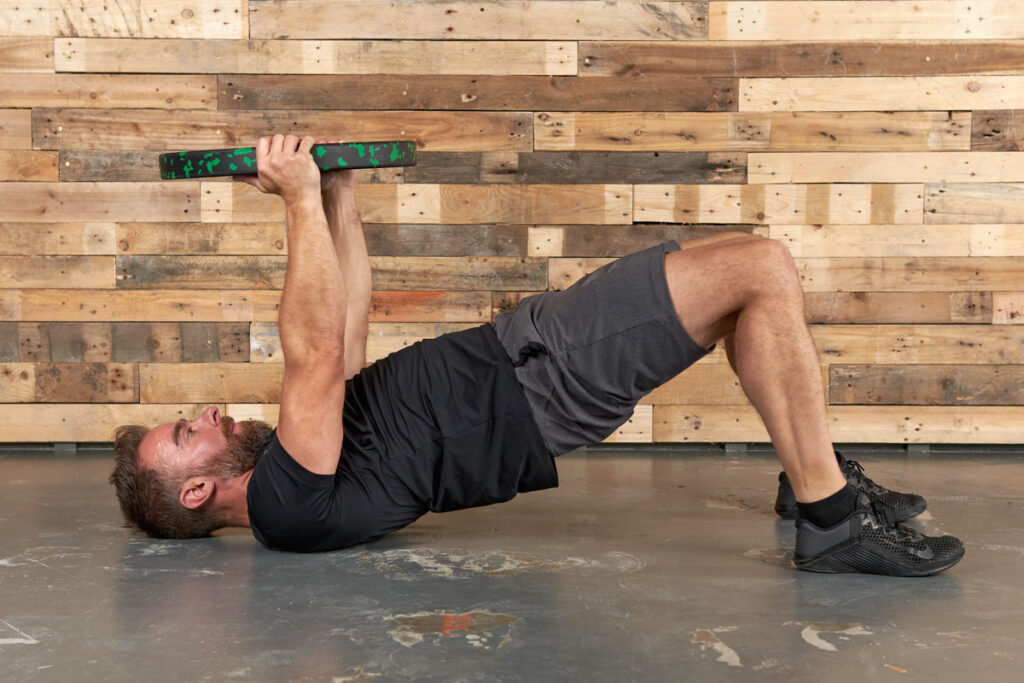Man performing a hip bridge with arm raise using a Mirafit 10kg weight plate