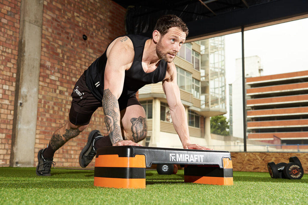 A man performs mountain climbers in a gym using a Mirafit Aerobic Exercise Step