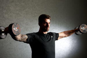 Man performing a dumbbell lateral raise with Mirafit 12.5kg Dumbbells