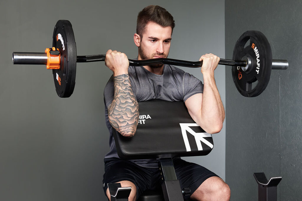 Man performing a preacher curl with a Mirafit Preacher Curl Bench, Mirafit M3 Olympic EZ Curl Bar and M3 Urethane Olympic Weight Plates