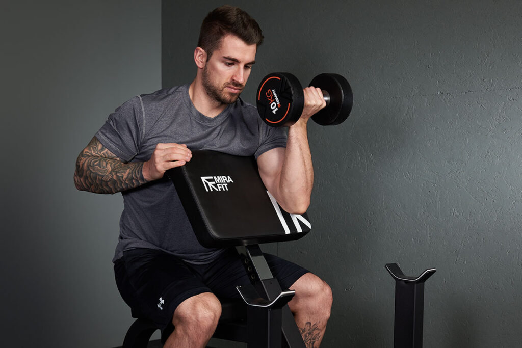 Man performing a preacher curl with a Mirafit Preacher Curl Bench and 10kg dumbbells