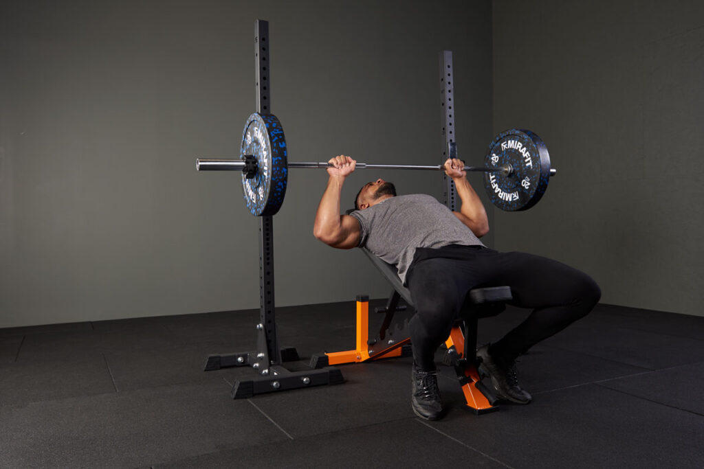 Man performing an incline bench press with a Mirafit adjustable weight bench and 20kg plates