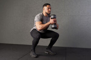 Man performing a squat using Mirafit 10kg dumbbell