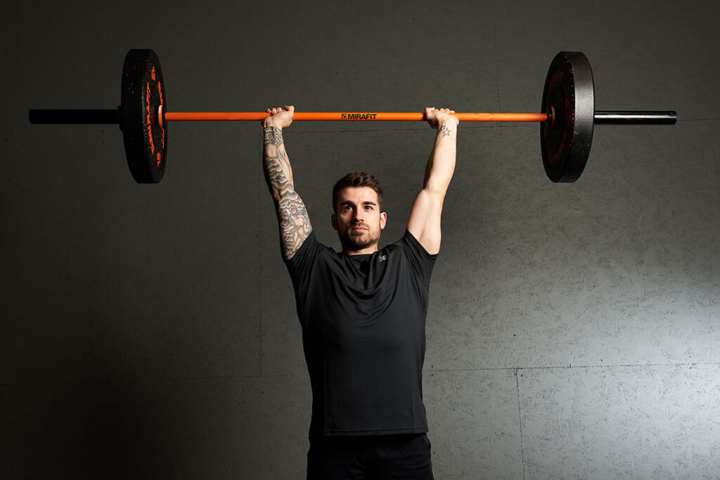Man performing a barbell military press with a Mirafit Olympic barbell and bumper plates.