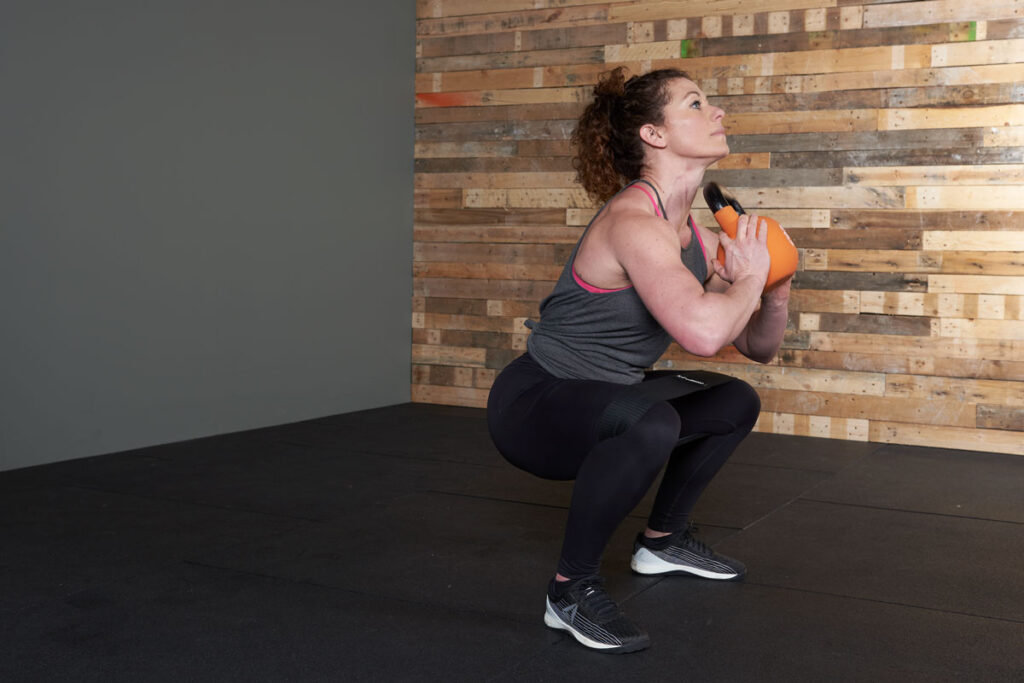 Woman performing a squat with a Mirafit fabric resistance band and a Mirafit kettlebell.