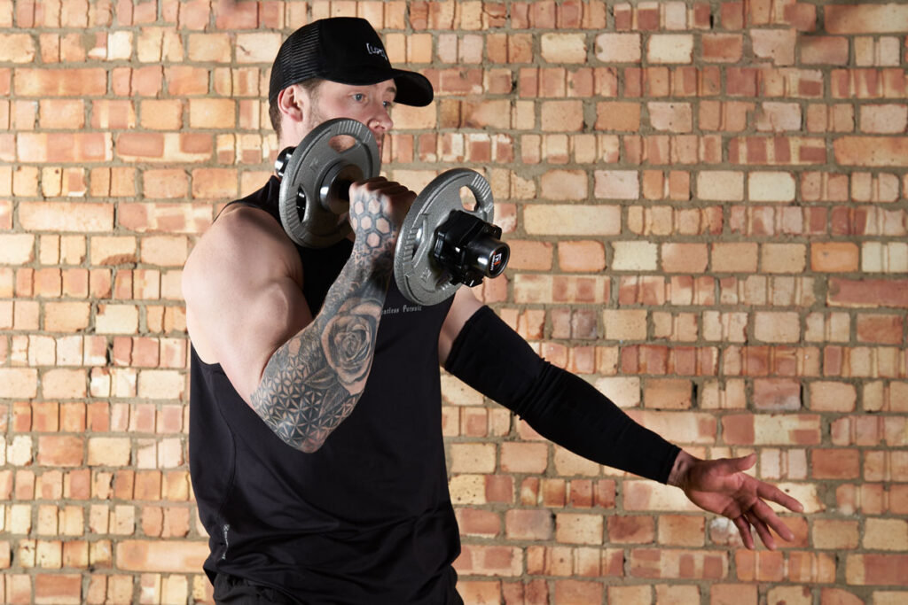 Single arm dumbbell snatch Man doing a single arm dumbbell snatch with Mirafit cast iron plates