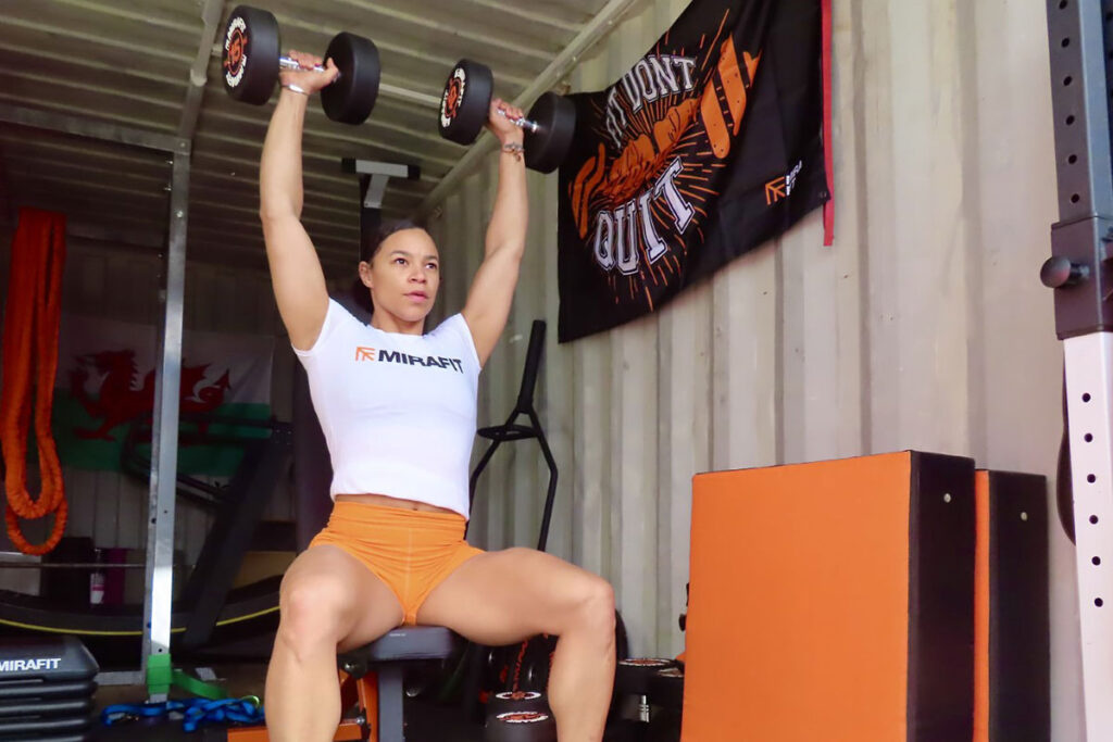Mica Moore with 15kg Dumbbells Mica Moore performing a dumbbell shoulder press using Mirafit 15kg dumbbells