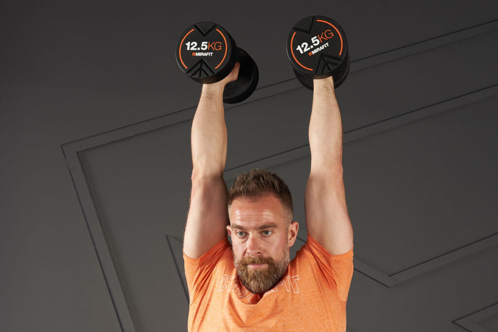 Dumbbell Curl to Press Man doing a dumbbell curl to press with Mirafit 12.5kg dumbbells