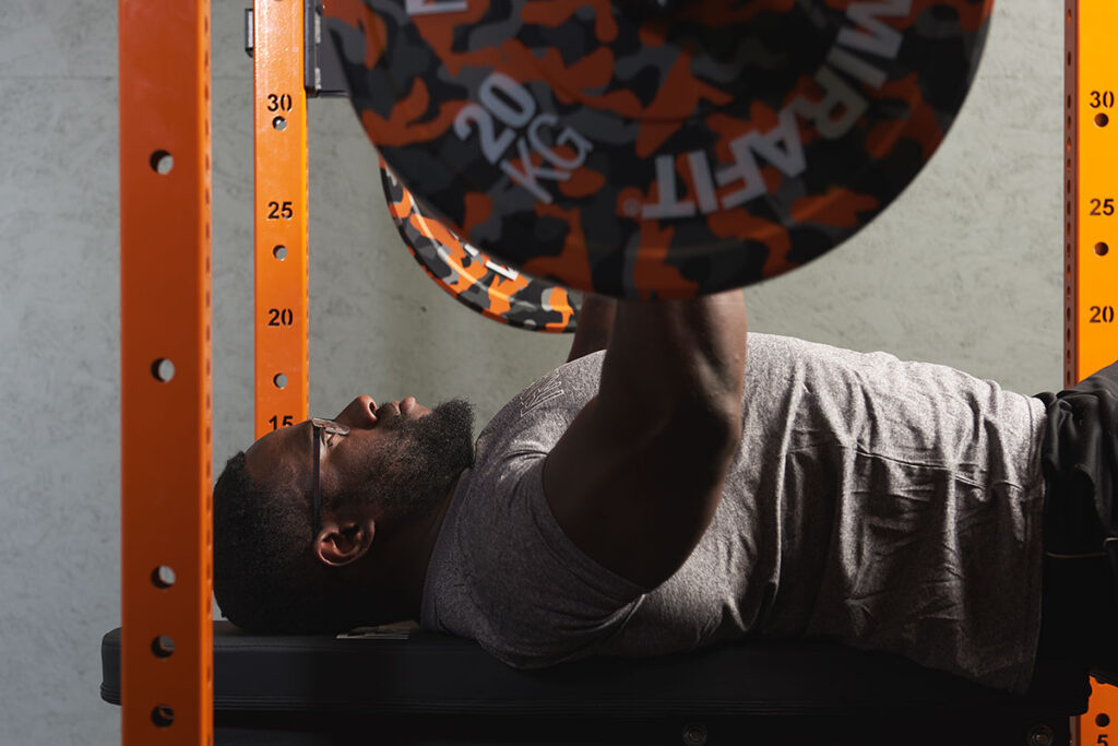 Man doing a flat bench press with Mirafit Orange Camo Bumper Plates