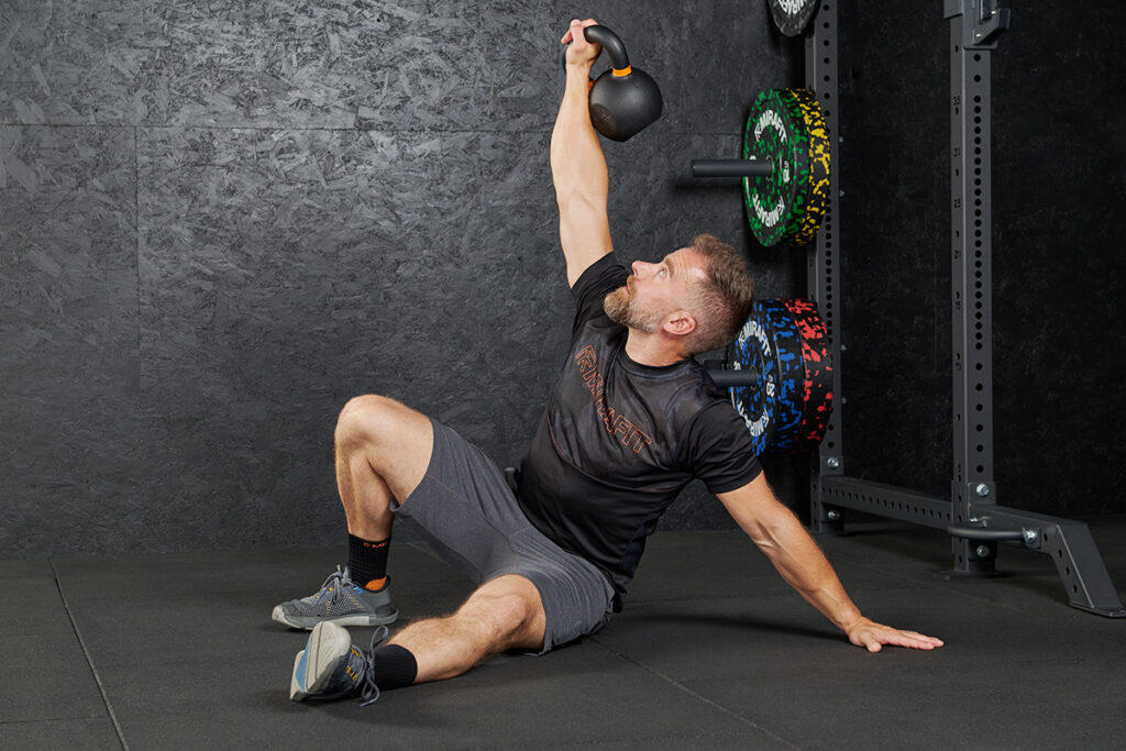 Turkish Get Up Man performs a functional kettlebell exercise, the Turkish Get Up with a Mirafit Cast Iron Kettlebell
