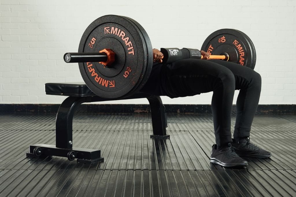 Man performing a barbell hip raise with 10kg weight plates and 5kg weight plates