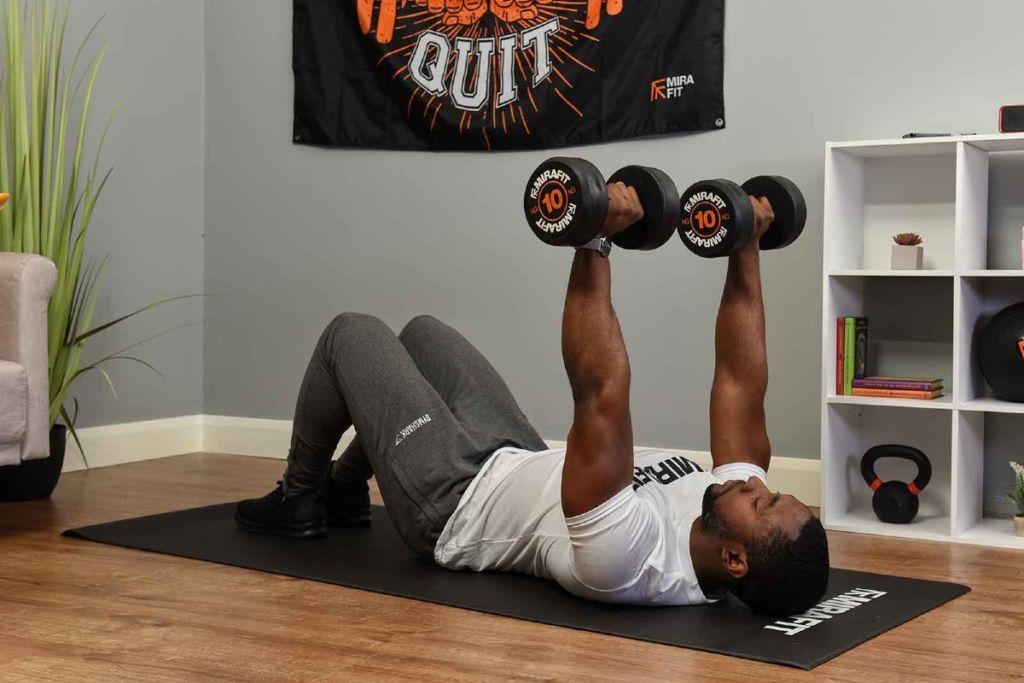This is an image of a fitness model demonstrating the dumbbell floor press exercise at home. 
