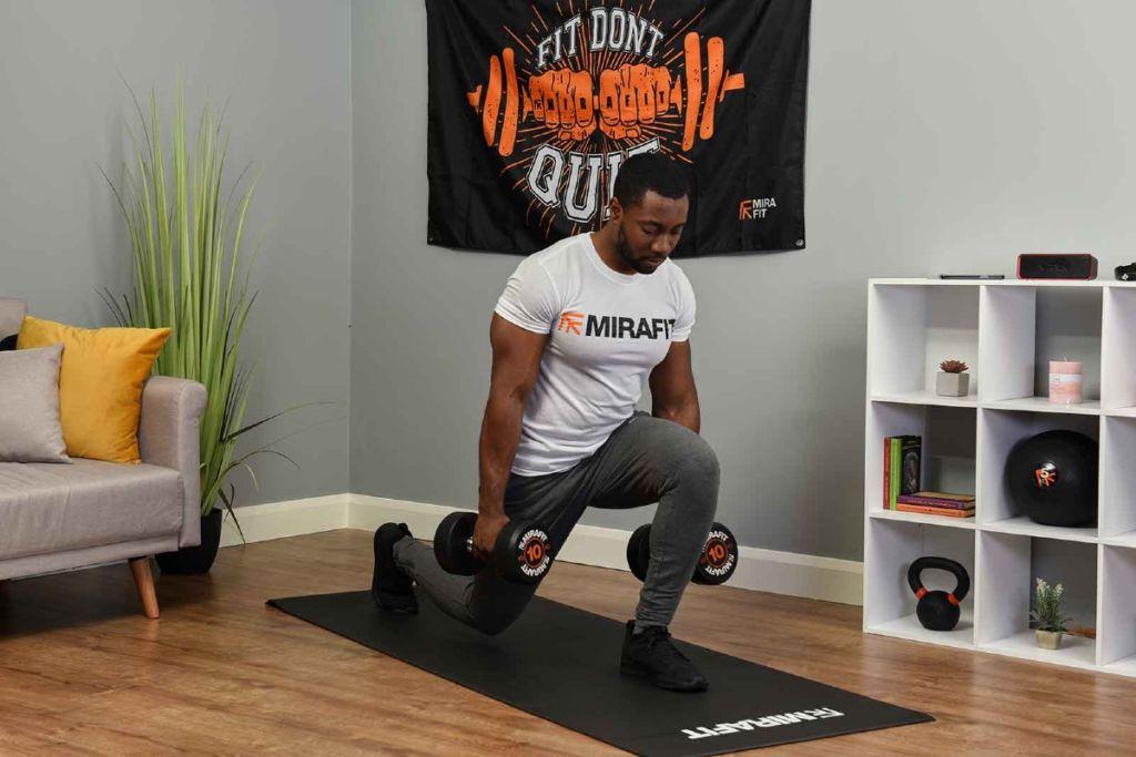 This is an image of a fitness model demonstrating the dumbbell lunge exercise on a yoga mat in his living room. 